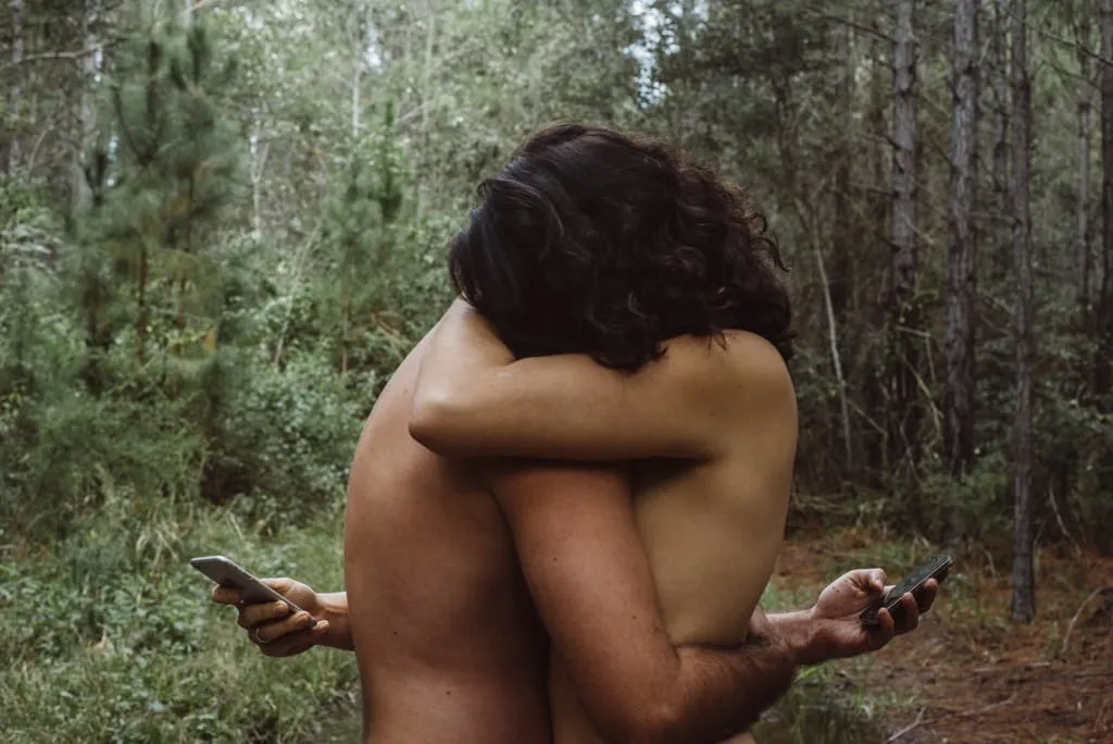 a man and a woman standing in the woods looking at their phones